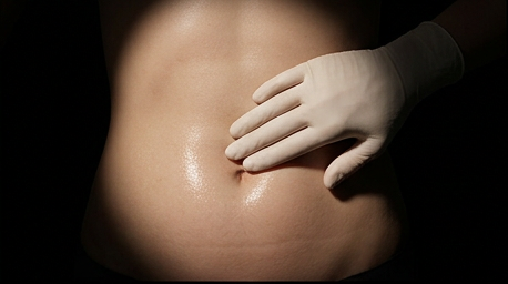 Clinician's hand palpating a bare abdomen, establishing shot